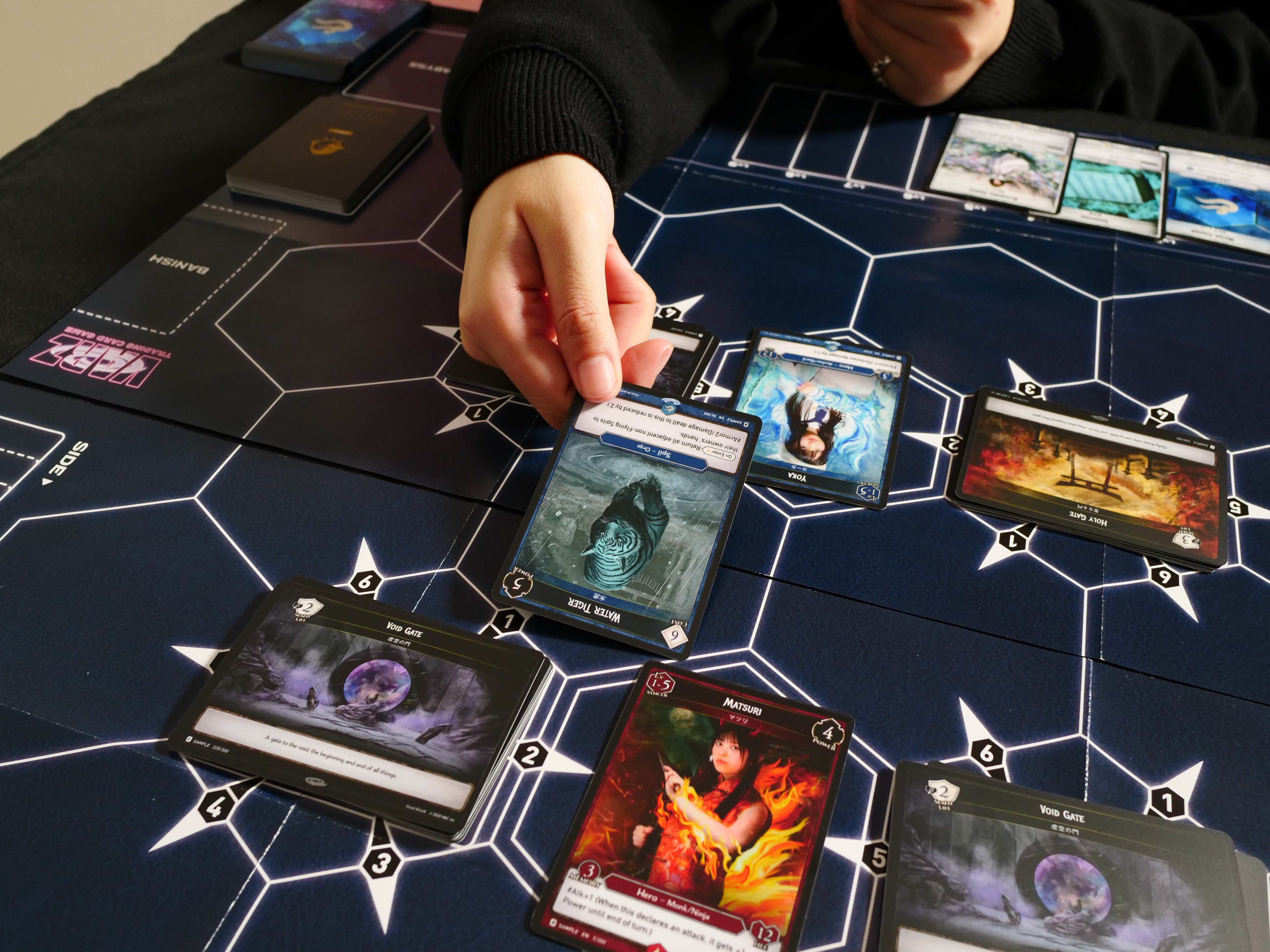 A player placing a Water Tiger card onto the hex battlefield during a VARZ match, with a hand of cards held nearby